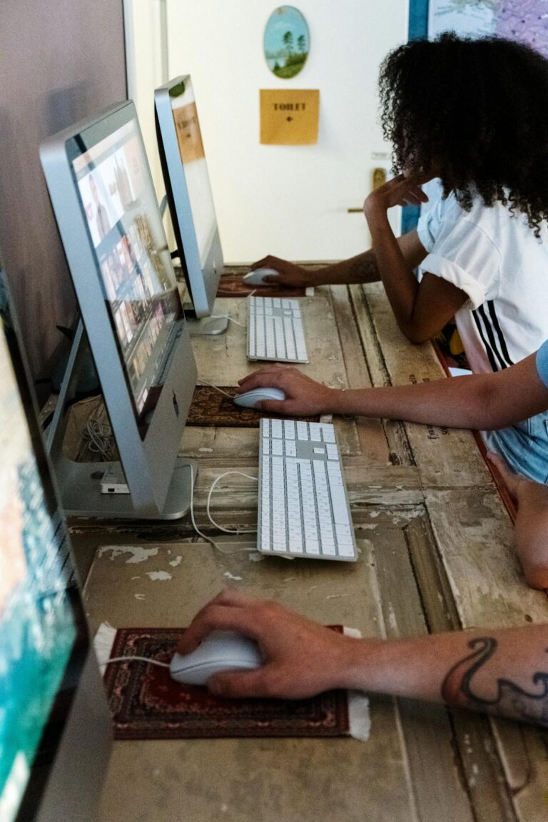 People using shared computers in a common room, working on various tasks online.